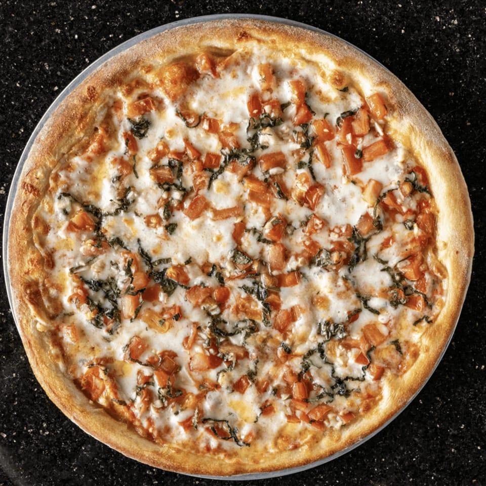 A whole white pizza with diced tomatoes and basil on a dark, speckled surface.