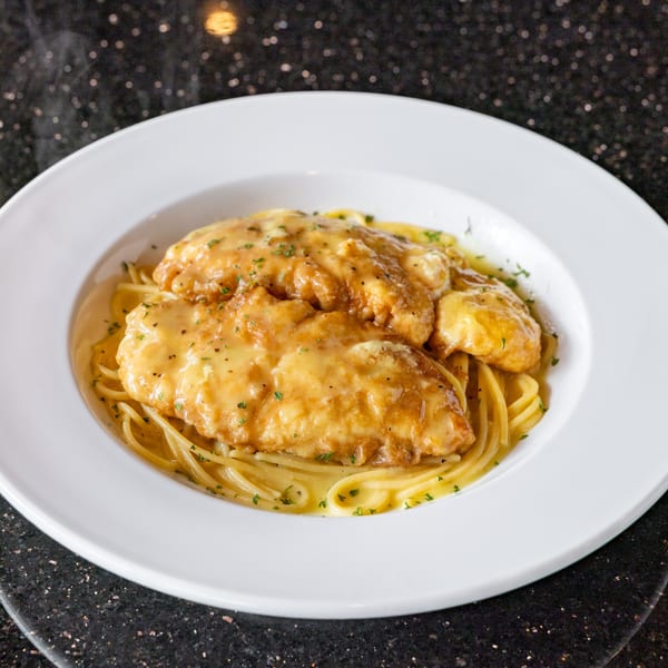 Chicken Alfredo pasta with creamy sauce and parsley in a white bowl on a dark speckled surface.