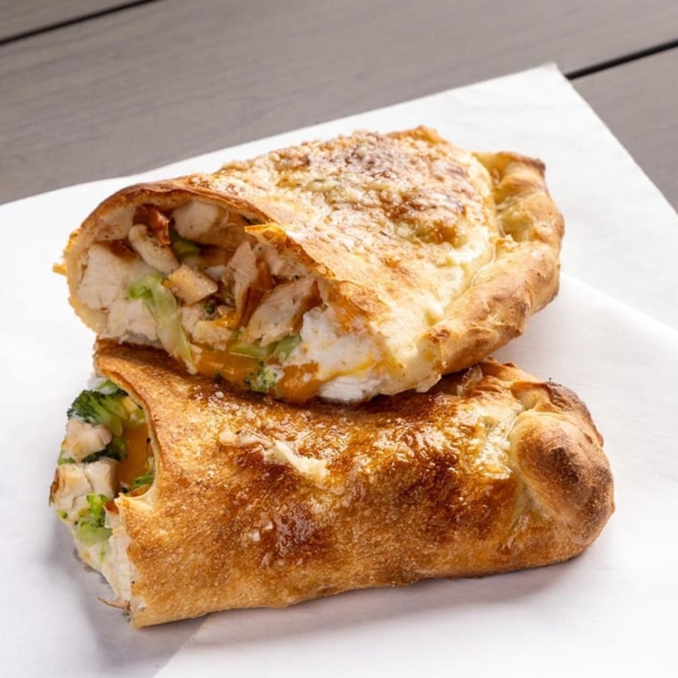 Two golden-brown calzones, one sliced open revealing chicken, broccoli, and cheese filling.