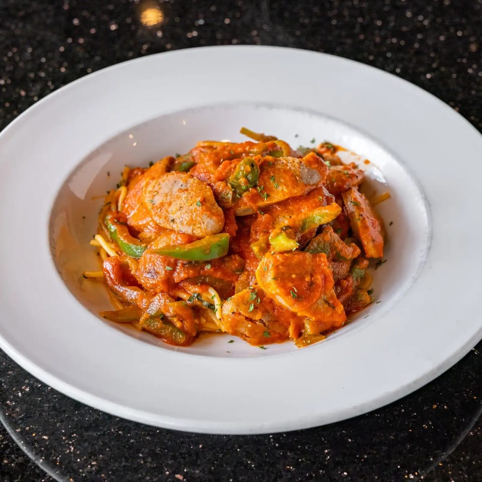 A white bowl filled with pasta, chicken, green peppers, and a rich red sauce.