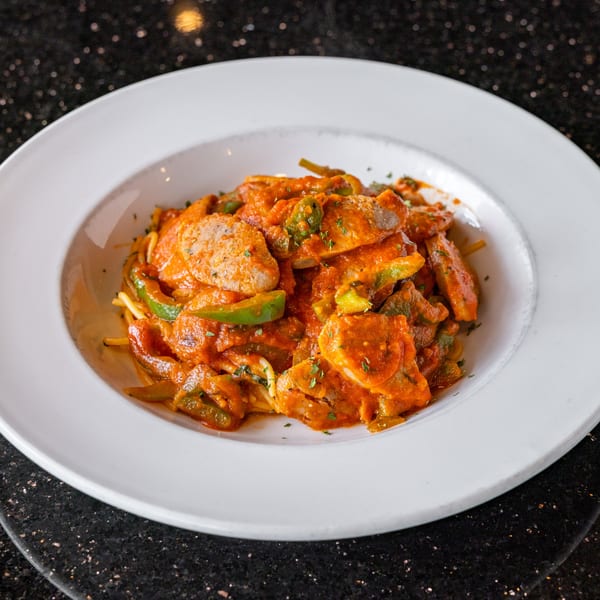 A white bowl filled with Grande Pizza's pasta, featuring sausage, green peppers, and red sauce.