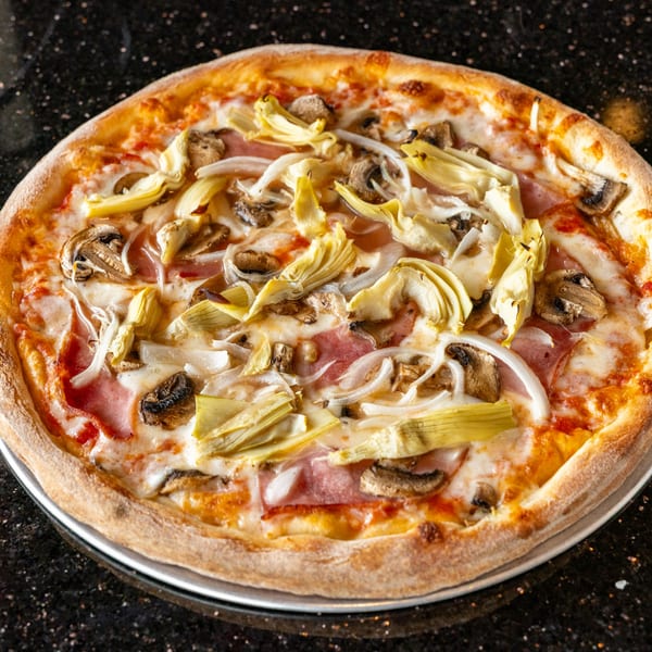 Grande Pizza's pizza with ham, artichokes, mushrooms, and onions on a dark countertop.