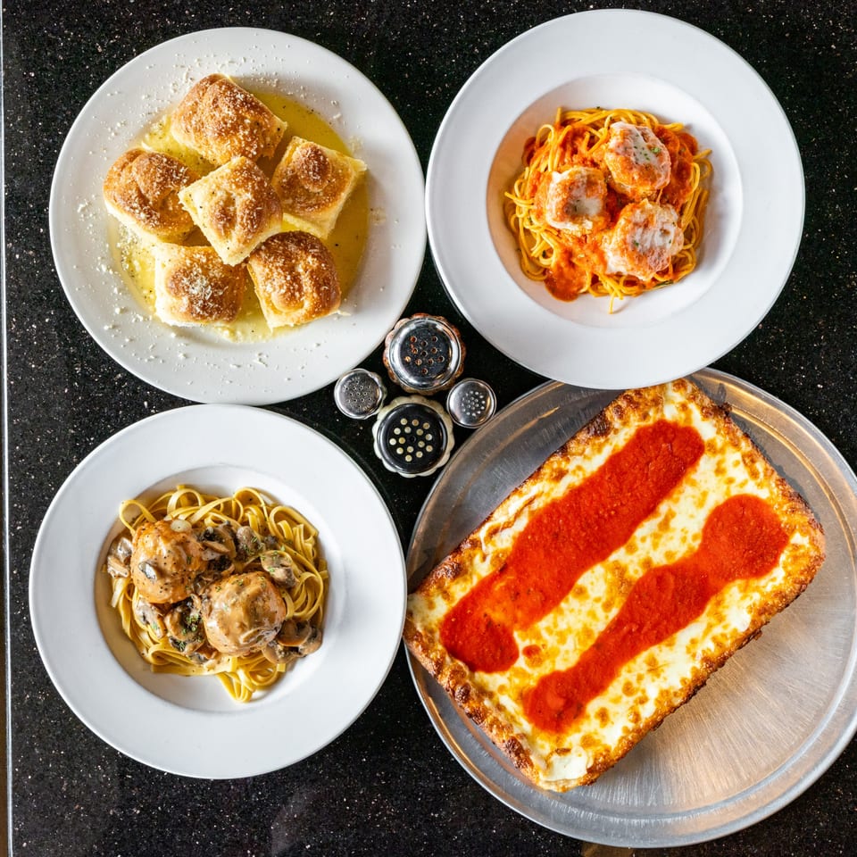 Overhead view of Grande Pizza's garlic knots, two pasta dishes with meatballs, and a rectangular pizza.