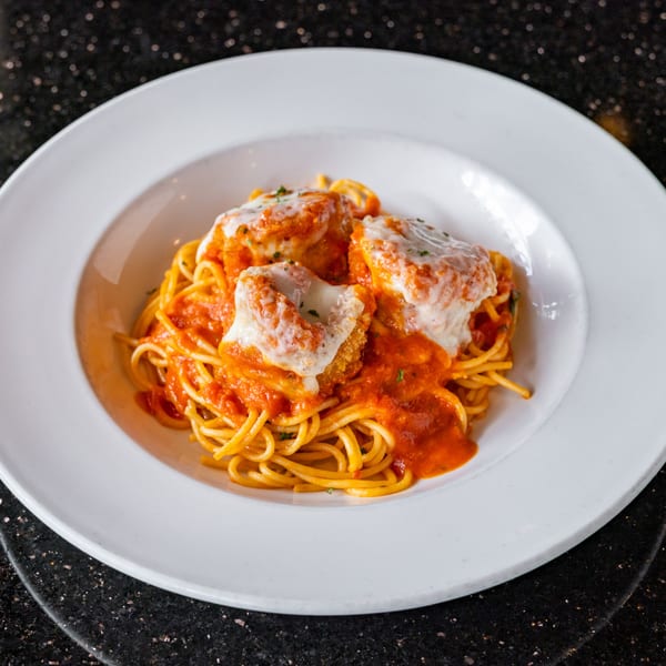 Spaghetti with red sauce and three breaded chicken cutlets topped with melted cheese in a white bowl.
