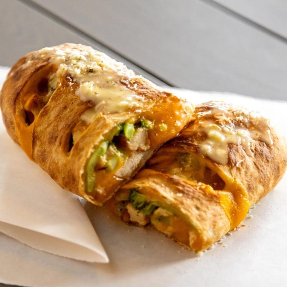 Two halves of a golden-brown calzone, filled with chicken and green vegetables, topped with melted cheese.